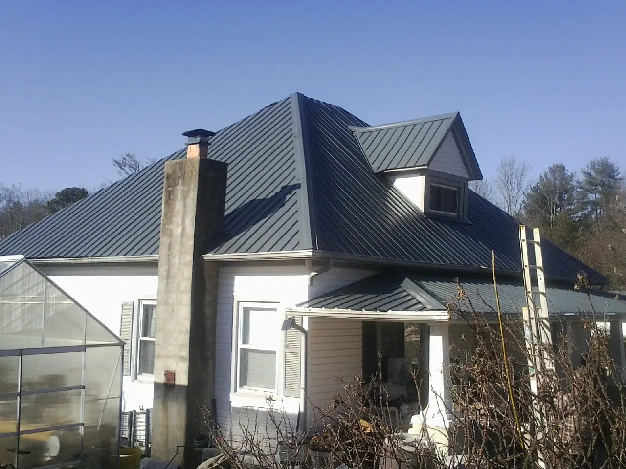 Dark blue standing seam metal roof on a white farmhouse with dormer — Slate & Tile Roof Repair by Roofing Brothers in Rayland