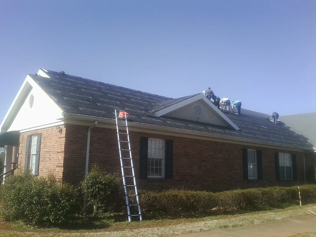 Crew tearing shingles off a brick ranch roof with a ladder set — Emergency Roof Repair work by our crew in Rayland