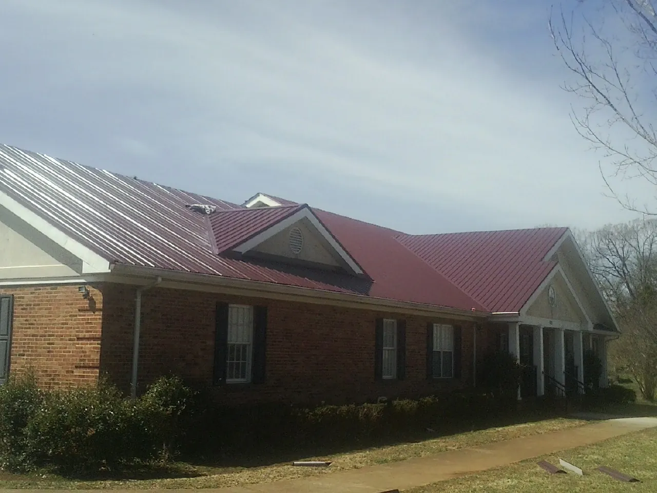 Red metal roof with gabled entries on a long brick building, from a Hail Damage Roof Repair job in Rayland