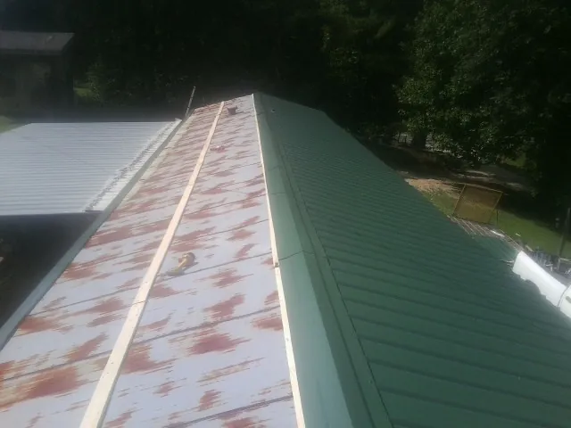 Old rusted panels beside newly installed green metal roofing — Wind Damage Roof Repair by Roofing Brothers in Rayland