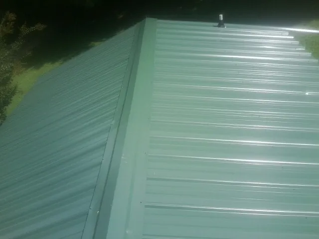 New green metal panels meeting at the ridge of a roof — Flat Roof Repair work by our crew in Rayland