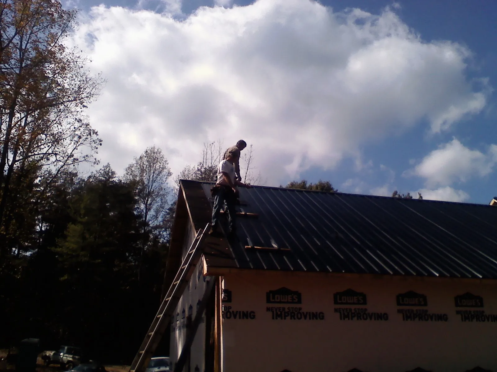 Roofer fastening dark metal panels high against a cloudy sky, from a Roof Inspection job in Rayland