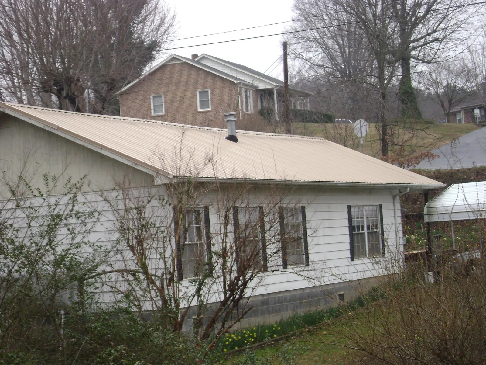 Tan metal roof on a white sided house set into a hillside — Commercial Roofing by Roofing Brothers in Rayland